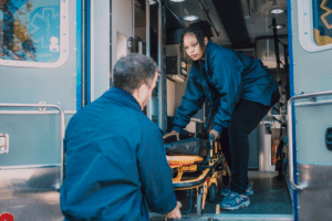A man and a woman are wheeling out an empty stretcher from the ambulance truck.